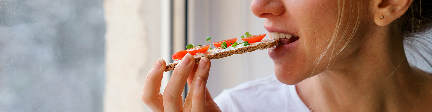 Mujer comiéndose una tostada con tomate y mirando por la ventana
