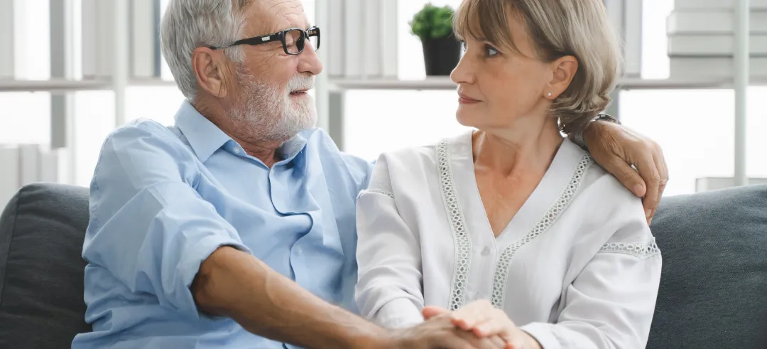 Pareja anciana sentados en el sofá de su casa y dándose las manos